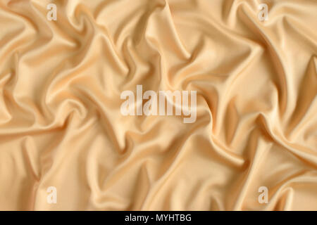 Close up of ripples in gold colored silk fabric. Satin textile background. Stock Photo