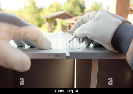 Furniture assembly. Worker in protective gloves measuring part of kitchen cabinet with construction ruler Stock Photo