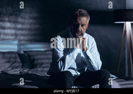 Stressed and depressed man sitting alone in the dark with a problem Stock Photo