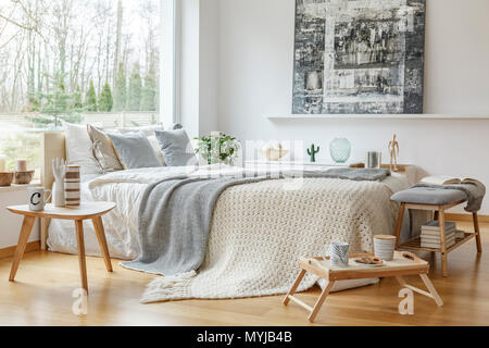 Painting on the wall in scandi bedroom interior with wooden furniture and knit blanket on bed Stock Photo