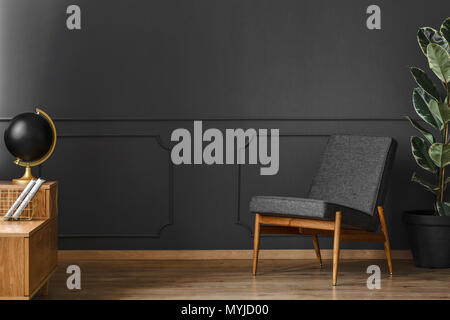 Spacious, black retro room interior with black walls, chair, wooden floor and cupboard Stock Photo