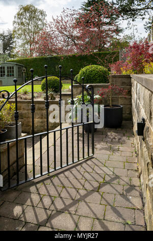 View through open gate to beautiful, landscaped, private garden with contemporary design, shrubs, box balls, path & neat lawn - Yorkshire, England, UK Stock Photo