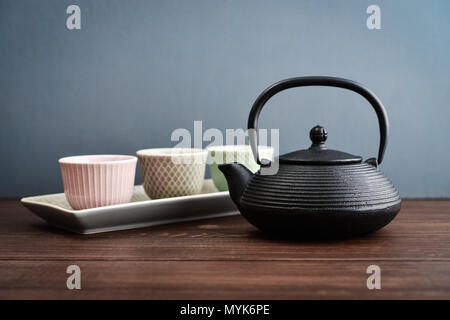 A set of Japanese-style dishes: iron teapot, cups and plate on a gray background Stock Photo
