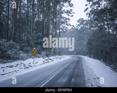 Slippery road warning sign for car drivers on side of a snow covered road. Icy scenic mountain route in winter forest. Mt Donna Buang, VIC Australia Stock Photo