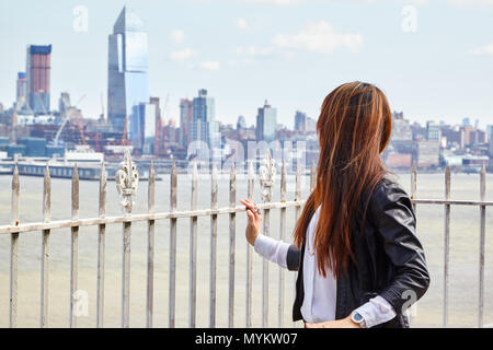 asian woman in leather jacket standing in front of city skyline Stock Photo