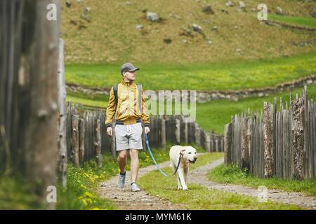 Tourist with dog in countryside. Young man walking with labrador retriever on dirt road. Stock Photo