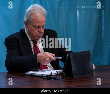 Elderly caucasian executive with grey hair and a dark suit works at a boardroom table image with copy space in landscape format Stock Photo