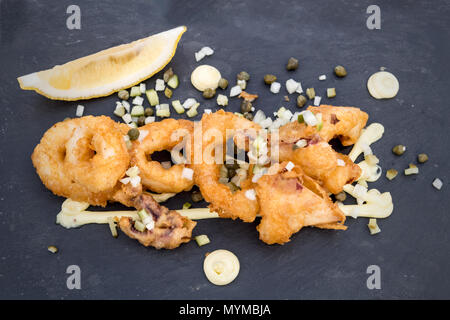 A delectable plate of golden fried calamari rings served with a slice of lemon, garnished with finely chopped onions, capers, Stock Photo