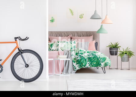 Black and orange bike standing in white bedroom with floral bedsheets Stock Photo