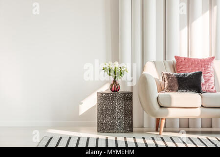White roses on metal table in bright living room interior with pink satin pillow on beige sofa Stock Photo