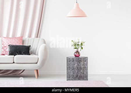 Metal table next to beige sofa with pink and gray pillow in bright interior of living room Stock Photo