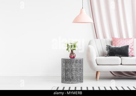 Roses on black table next to bright sofa with cushions in living room interior with empty wall Stock Photo