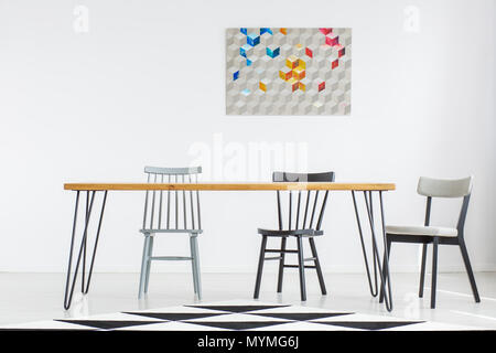 Colorful poster on white wall in dining room with geometric carpet and chairs at wooden table Stock Photo