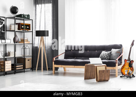 Laptop placed on a modern table standing by the black sofa in man living room interior with window Stock Photo