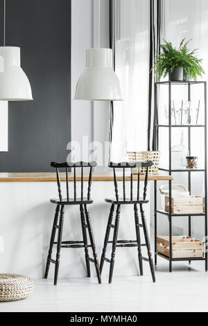 Plant on black shelf next to black bar stools at countertop with white lamps in rustic dining room Stock Photo