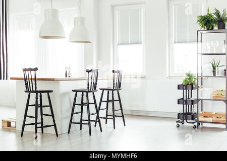 White lamps above kitchen island under a window with black bar stools in bright room with plants Stock Photo