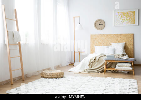 Modern clock hanging over a double bed filled with pillows in a white bedroom interior Stock Photo