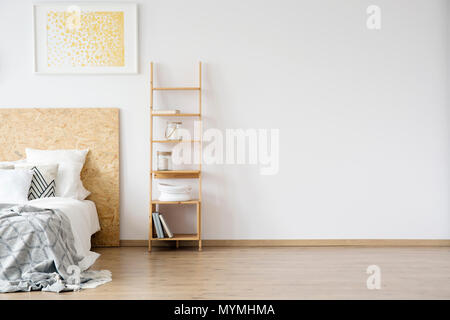 Glass jars on shelves against white wall with copy space in simple bedroom with gold painting above bed Stock Photo