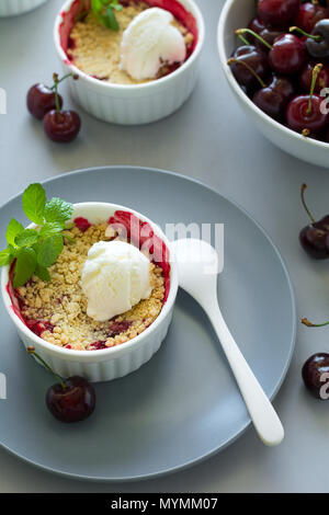 Cherry crumble with oatmeal and ice cream in bowl on grey wooden desk. Summer healthy food Stock Photo