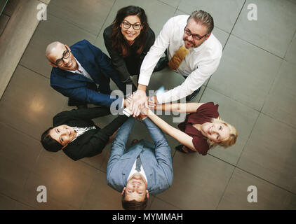 Top view of multi-ethnic business people putting their hands on top of each other and looking upwards. Business team making a stack of hands showing u Stock Photo