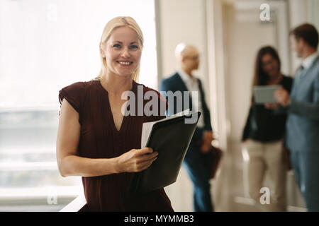 Happy business woman with coworkers talking in background. Female manager with colleagues at the back. Stock Photo
