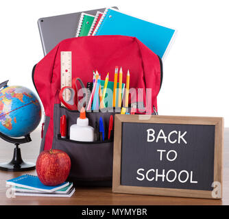 Backpack with an assortment of school supplies with BACK TO SCHOOL written on a chalkboard on a wooden desktop and white background Stock Photo
