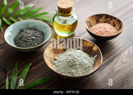 Different cosmetic clay in coconut bowl and massage oil on wooden background closeup Stock Photo