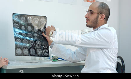 Smiling doctor showing brain computed tomography x-ray image to his patients Stock Photo