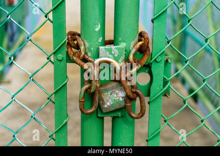 Old and rusty padlock chained to a green door in a fence restricting access to a small bridge Stock Photo