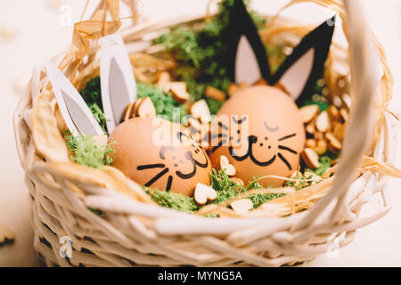 Two smiling bunnies laying in the basket with grass and wooden hearts. Easter egg. Stock Photo