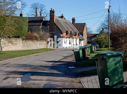 Church Street, West Hanney, Oxfordshire, UK. Wheelie bins await emptying in the foreground with the 17th century Plough Inn in the background. Stock Photo