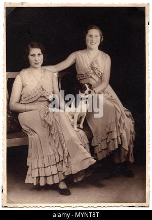 Two sisters (twins?) wearing identical dresses, with a pet terrier dog between them.  Photograph made in the 1930s.  On the reverse is written 'Hilsen til Helen fra Sonja og Gudrun Bendsen'  (Greetings to Helen from Sonja and Gudrun Bendsen) Stock Photo