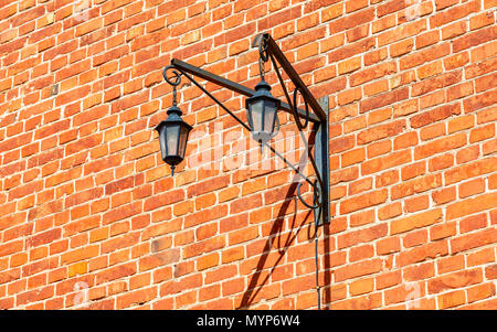 Old decorative iron street lamp hanging on the weathered brick wall Stock Photo