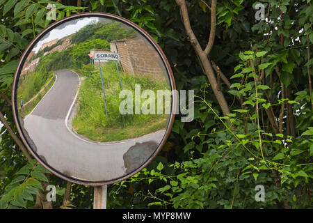view through round mirror of winding road to the ancient medieval hill town Sorano, Tuscany,  Italy in May Stock Photo