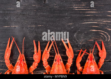 Three red boiled crayfish lie in the half on a wooden dark background Stock Photo