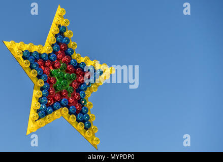 Colorful shining star from many single lamps with different colors on a fair, exempted before a blue sky, isolated Stock Photo