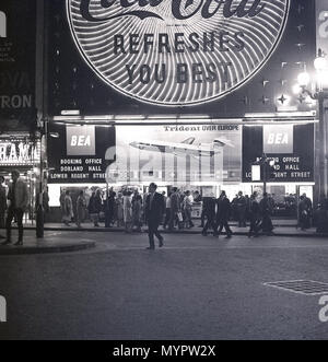 1960s, historical, eveningtime in London's West End and people at Piccadilly Circus at Lower Regent Street outside retail outlets, with the neon billboards lighting up the area. An advertising billboard for the Trident aircraft from British European Airways (BEA) can be seen in the picture. Stock Photo