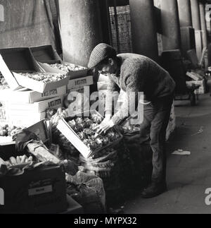 1960s, historical, eveningtime and in London's Covent Garden, a market trader checking his display of fresh vegetables. Stock Photo