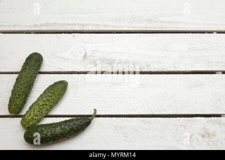 three green fresh cucumbers on white wooden garden table, left side of the frame Stock Photo