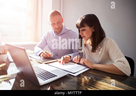 Two Happy Businesspeople Working On Document With Laptop On Desk Stock Photo