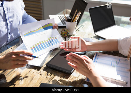 Businessman's Hand Showing Graph To His Colleague Over Wooden Desk Stock Photo