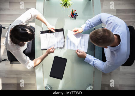 Elevated View Of Two Businesspeople Holding Resume Over Desk In Office Stock Photo