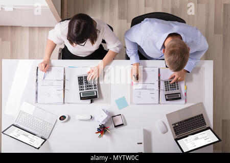Two Young Businesspeople Calculating Invoice With Calculator Stock Photo