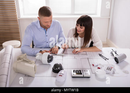 Two Architects Working On Blueprint With Security Equipments On Desk Stock Photo