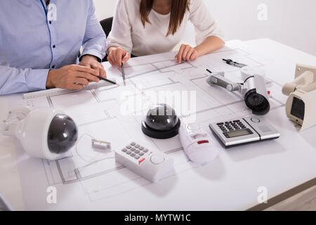 Various Security Equipments In Front Of Two Architects Planning Project On Blueprint Stock Photo
