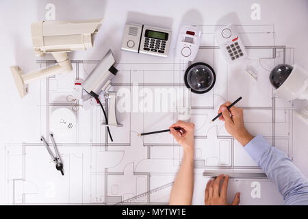 Various Security Equipments In Front Of Two Architects Planning Project On Blueprint Stock Photo