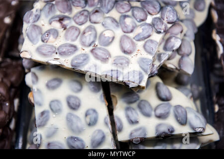 Macro closeup of pile of many white chocolate pieces chunks bars with peanuts, almonds on tray display in candy store chocolatier shop Stock Photo