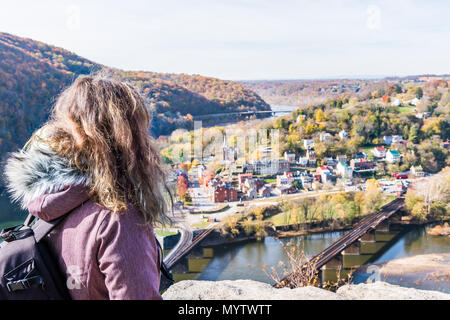 Overlook, hiker woman girl looking at cityscape, colorful orange yellow foliage fall autumn forest with small village town by river in Harpers Ferry,  Stock Photo