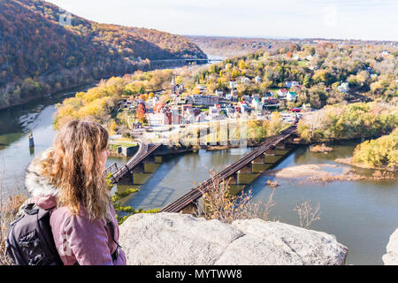 Hiker woman girl looking at cityscape overlook, colorful orange yellow foliage fall autumn forest with small village town by river in Harpers Ferry, W Stock Photo