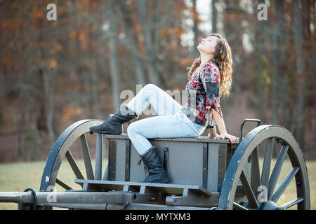 Young happy woman sitting on old cannon carriage in Manassas National Battlefield Park in Virginia where Bull Run battle was fought, sunlight Stock Photo